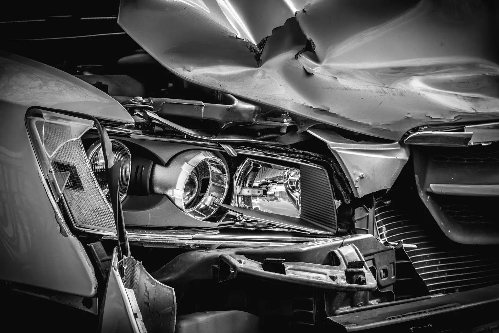 Close view of a silver car's crushed hood and broken headlight after a front-end crash